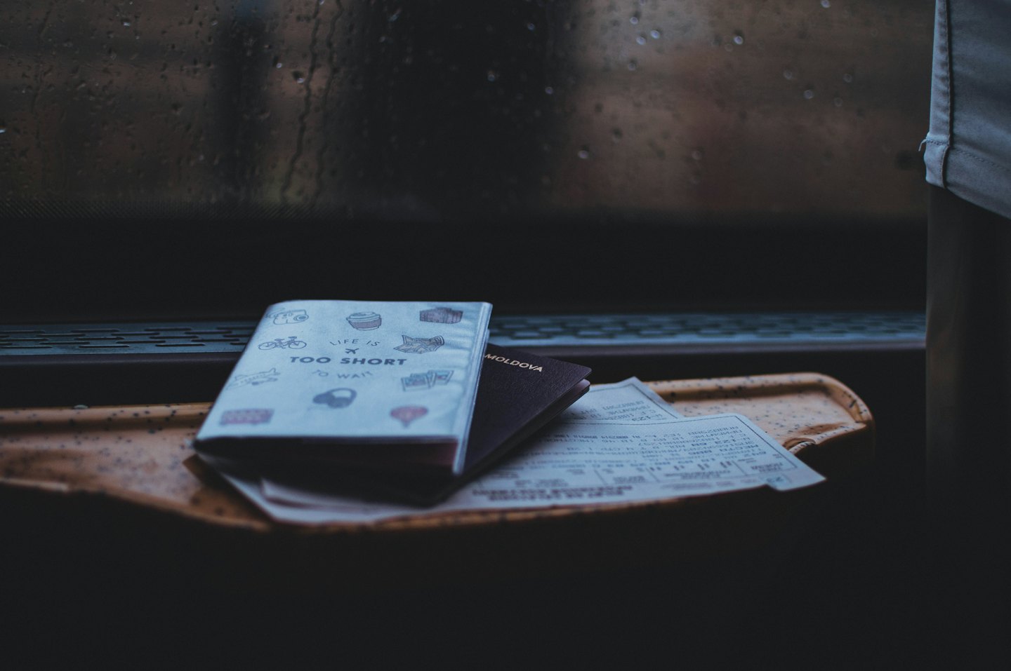 Two passports and tickets on a yellow tray next to a rainy window.