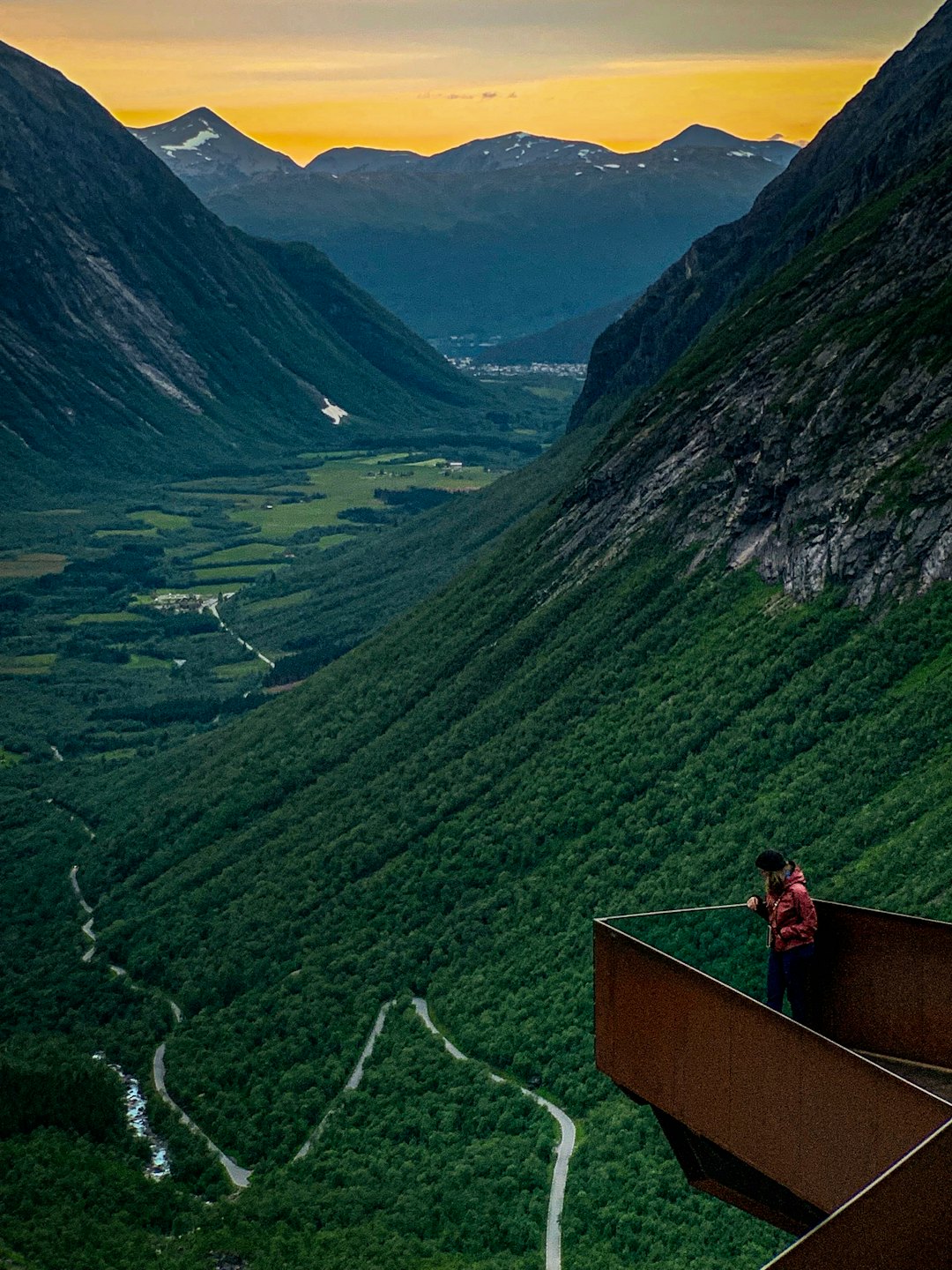 A traveler stands on a viewpoint overlooking a forested mountain valley.