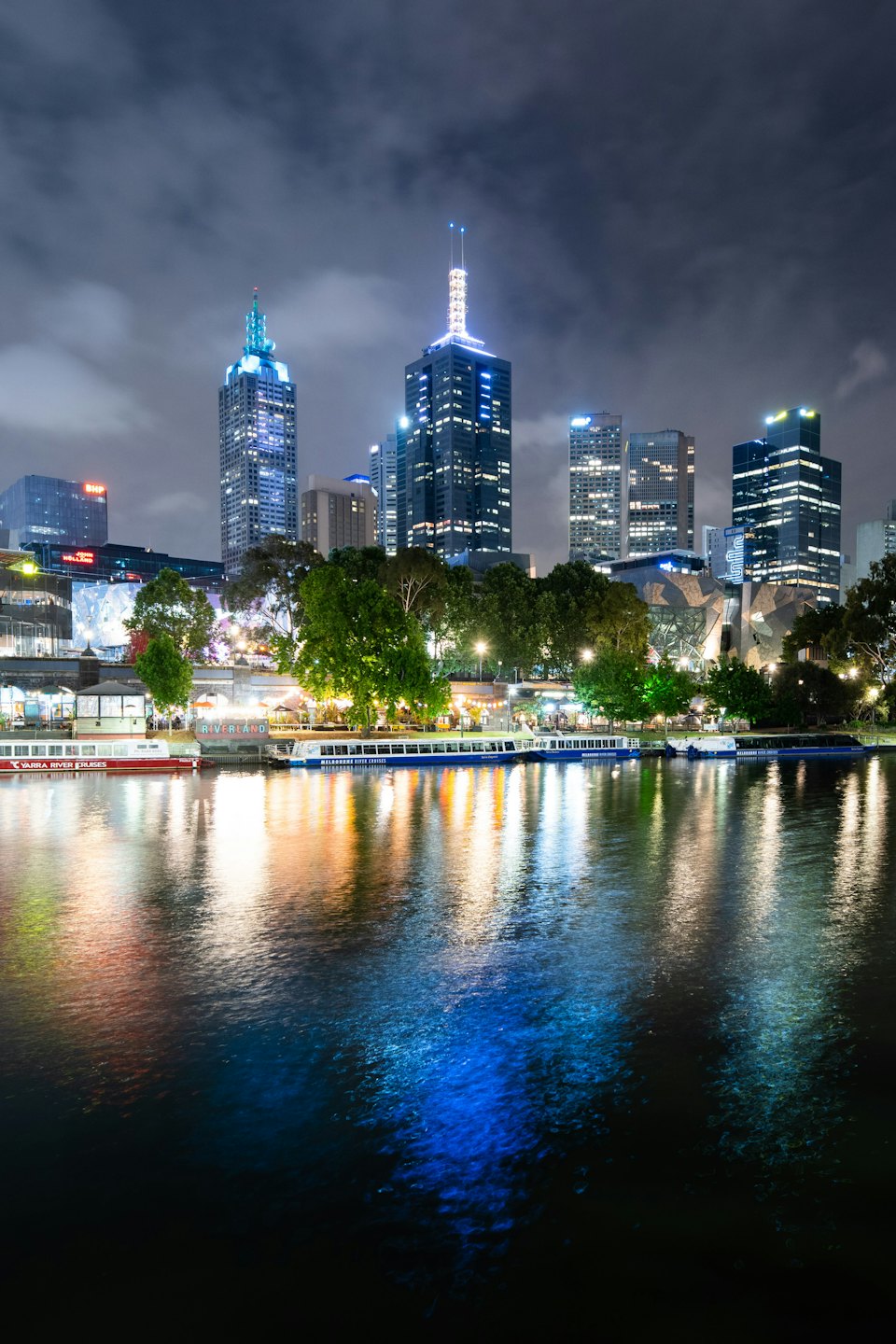 Illuminated city skyscrapers reflect on the calm river at night.