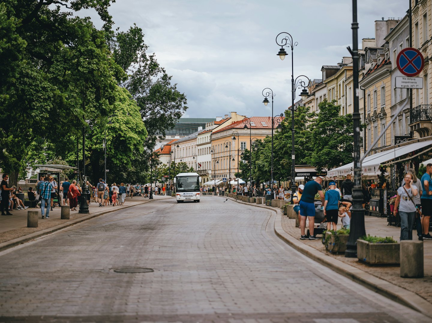 Pedestrians walk along a bustling European street with historic buildings.